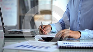 Company marketer counting calculator and filling report, sitting at office table