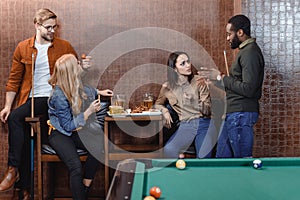 company of multiethnic friends eating and drinking beside pool table