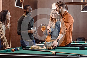 company of multiethnic friends eating and drinking beside pool table