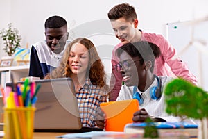 Company of teenagers using laptop and tablet while studying together