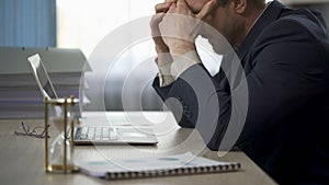 Company worker sitting at office desk, rubbing temples, tiredness, overtime work