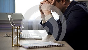 Company worker sitting at office desk, rubbing temples, tiredness, overtime work