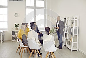 Company's senior business manager instructs subordinates at working meeting in office.