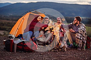 Company of young friends having a picnic by the mountains, they are chatting, laughing, drinking energy drink and bake