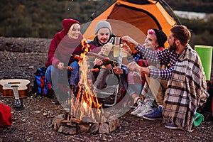 Company of young friends having a picnic by the mountains, they are chatting, laughing, drinking energy drink and bake