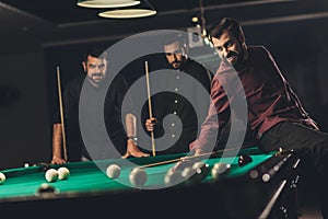 company of young successful handsome men playing in  russian pool