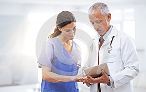 Comparing medical records. Shot of two medical professionals looking at a digital tablet.