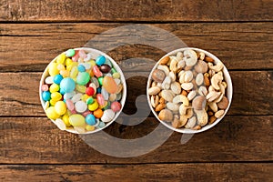 Comparison of healthy and unhealthy snacks. Mixed nuts and sweet in bowls on wooden background