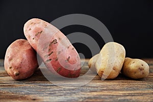 Comparison of sweet potatoes batata and ordinary potatoes on rustic wooden table with black background.