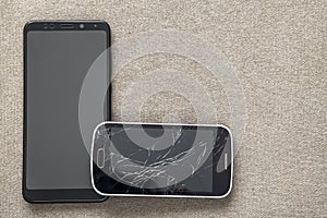 Comparison of two black mobile phones, old cellphone with cracked screen and new modern on light cloth copy space background.