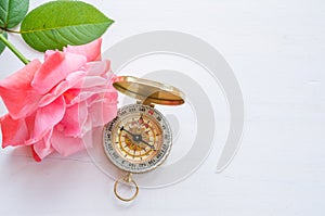 Compass with beautiful pink rose on a white wooden background