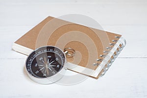 Compass and brown notebook on white wooden table background, journey planning concept