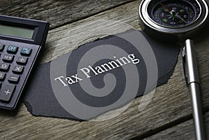 Compass,calculator,pen and a piece of black paper written with Tax Planning on wooden background