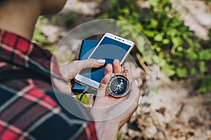 Compass in a girl s hand with a Smartphone and a Power Bank. Against the background of grass and sand