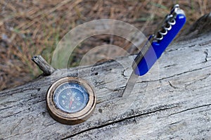 Compass and knife for survival in forest on log.