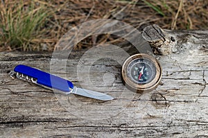 Compass and knife for survival in forest on log.