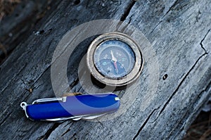 Compass and knife for survival in forest on log.