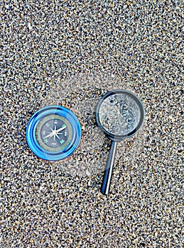 Compass and magnifier on sand