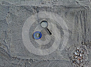 Compass and magnifier on sand