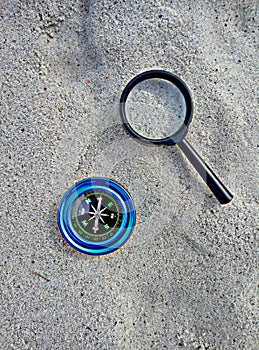 Compass and magnifier on sand