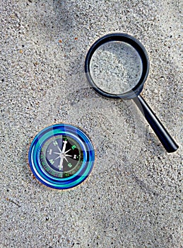 Compass and magnifier on sand