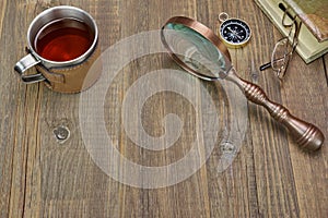 Compass, Magnifying Glass, Tea Mug, Two Notebooks on Wood Table