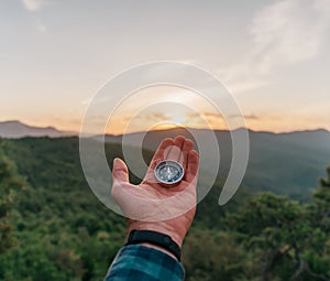 Compass on palm hand in summer mountains at sunrise.