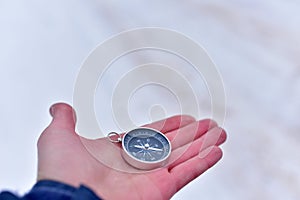 Compass in a man`s hand on the background of snow in the fores. Terrain orientation using a magnetic compass. Map reading and lan