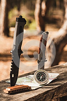 Compass, map, harmonica and knife on a wooden table in the woods, outdoor recreation.