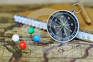 Compass, notebook and marking pins on blur vintage world map, journey concept