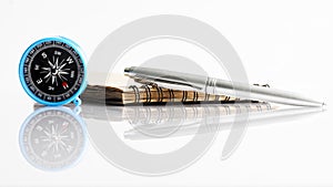 Compass, pen and notepad on a white reflective background. Vacation planning concept, travel or tourist trip