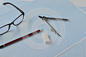 Compass, pencil, and eraser points on the blue graph paper for sketching.
