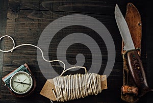 A compass, rusty hunting bushcraft knife and a linen rope on the wooden table. photo