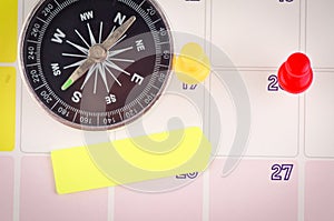 Compass, sticky paper and thumbtacks on calendar for planning concept background.