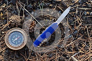 Compass and survival knife on background of earth.