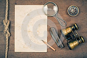 Compass, vintage binoculars, paper, old pocket knife, pencil, magnifying glass on wooden background