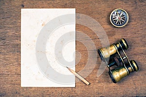 Compass, vintage binoculars, paper, pencil on wooden background