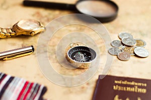 Compass on vintage world map with coins, pen, wrist watch, plane and flag for vacation and travel concept