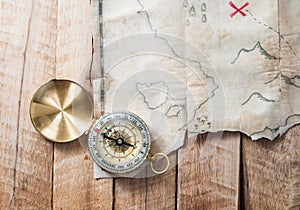 Compass on wooden desk with fake pirates treasure old map with red mark cross