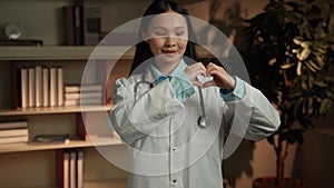 Compassionate Asian Female Doctor Gesturing Heart Sign in Clinic Office