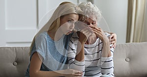 Compassionate young blonde woman cuddling stressed crying mother.