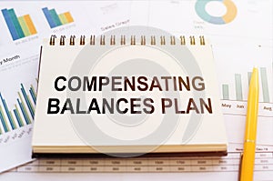 COMPENSATING BALANCES PLAN written on notepad on financial charts and graphs with yellow pen