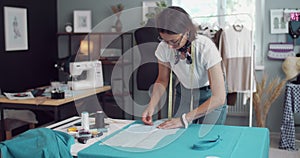 Competent dressmaker working with pattern on blue fabric