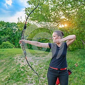 Competition in archery in nature. A young attractive woman points an arrow at a target