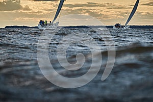 Competition of two sailboats on the horizon in sea at sunset, the amazing storm sky of different colors, race, big waves