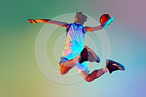 Competitive man, athlete in motion, training, playing basketball against gradient background in neon light