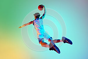 Competitive man, athlete in motion, training, playing basketball against gradient background in neon light