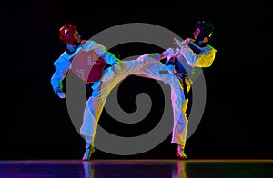 Competitive strong young men, taekwondo, karate athletes in motion, fighting, training against black background in neon