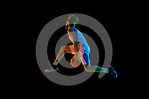 Competitive young man, basketball player in mid-air, training, jumping with ball against black background in neon light