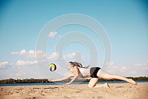 Competitive young woman athlete playing beach volleyball, hitting ball with hands and falling down on sand. Match